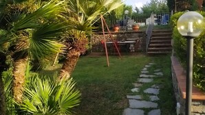 A garden pathway with palm trees, a stone wall, and a staircase leading to a deck area.