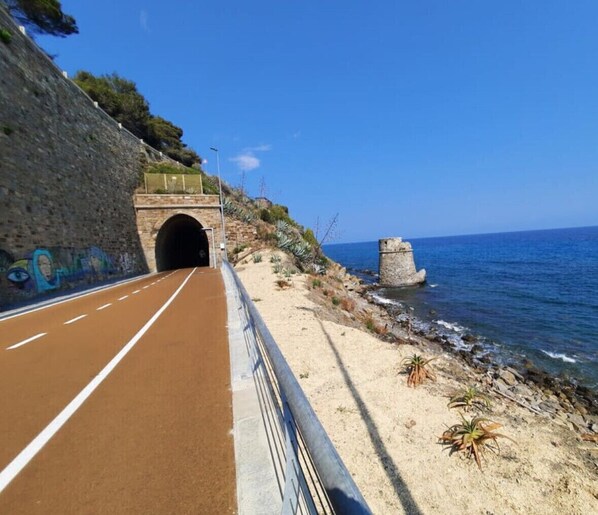 Une route côtière avec l’entrée d’un tunnel, un sentier longeant la plage et un promontoire rocheux près de la mer.