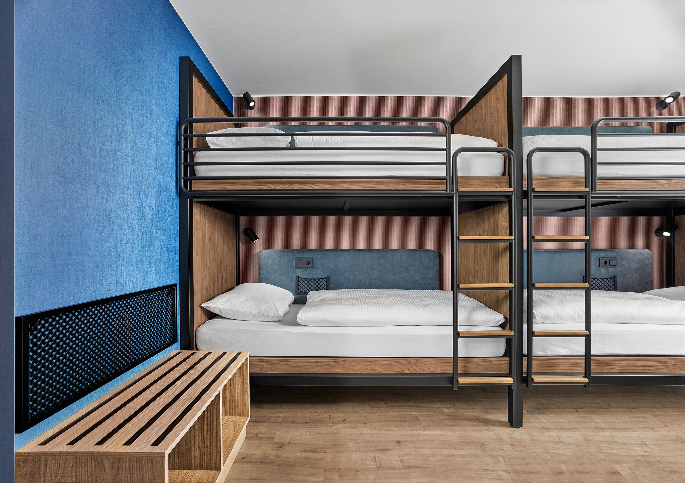 Habitación con literas, un banco de madera, una escalera y un cabecero con diseño de malla.