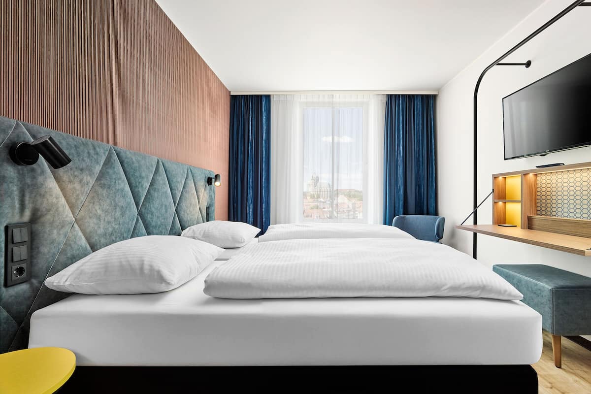 Quarto de hotel moderno com uma cama grande, televisão e vista para a cidade.