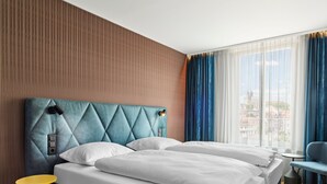 A hotel room with a large bed, a small table, and a view of the city through the window.