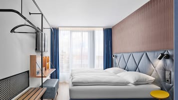 A modern hotel room with a bed, bench, bedside table, and a view of the city through large windows.