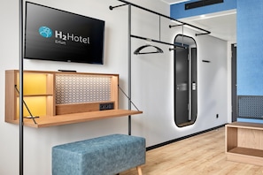 Une chambre d’hôtel moderne équipée d’un téléviseur fixé au mur, d’une étagère en bois à motifs alvéolaires, d’un banc bleu et d’une barre de traction.