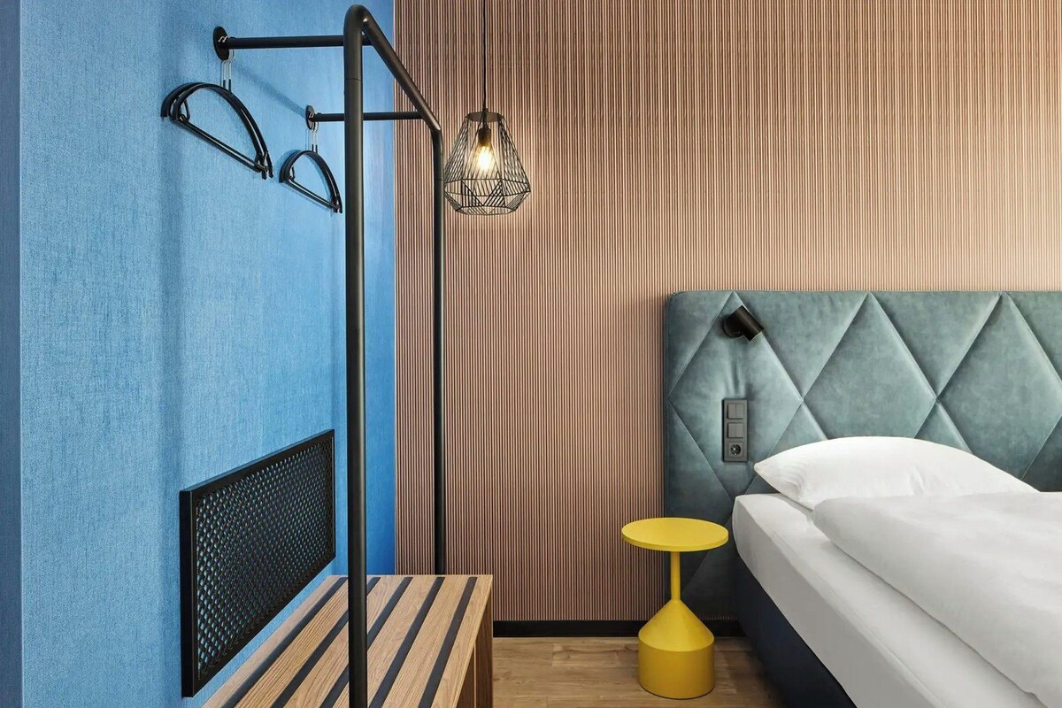 Un dormitorio con cama, mesita de noche, lámpara colgante y radiador.