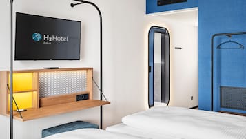A hotel room with a bed, a TV mounted on a wall, a wooden shelf with a radio, and a mirror.