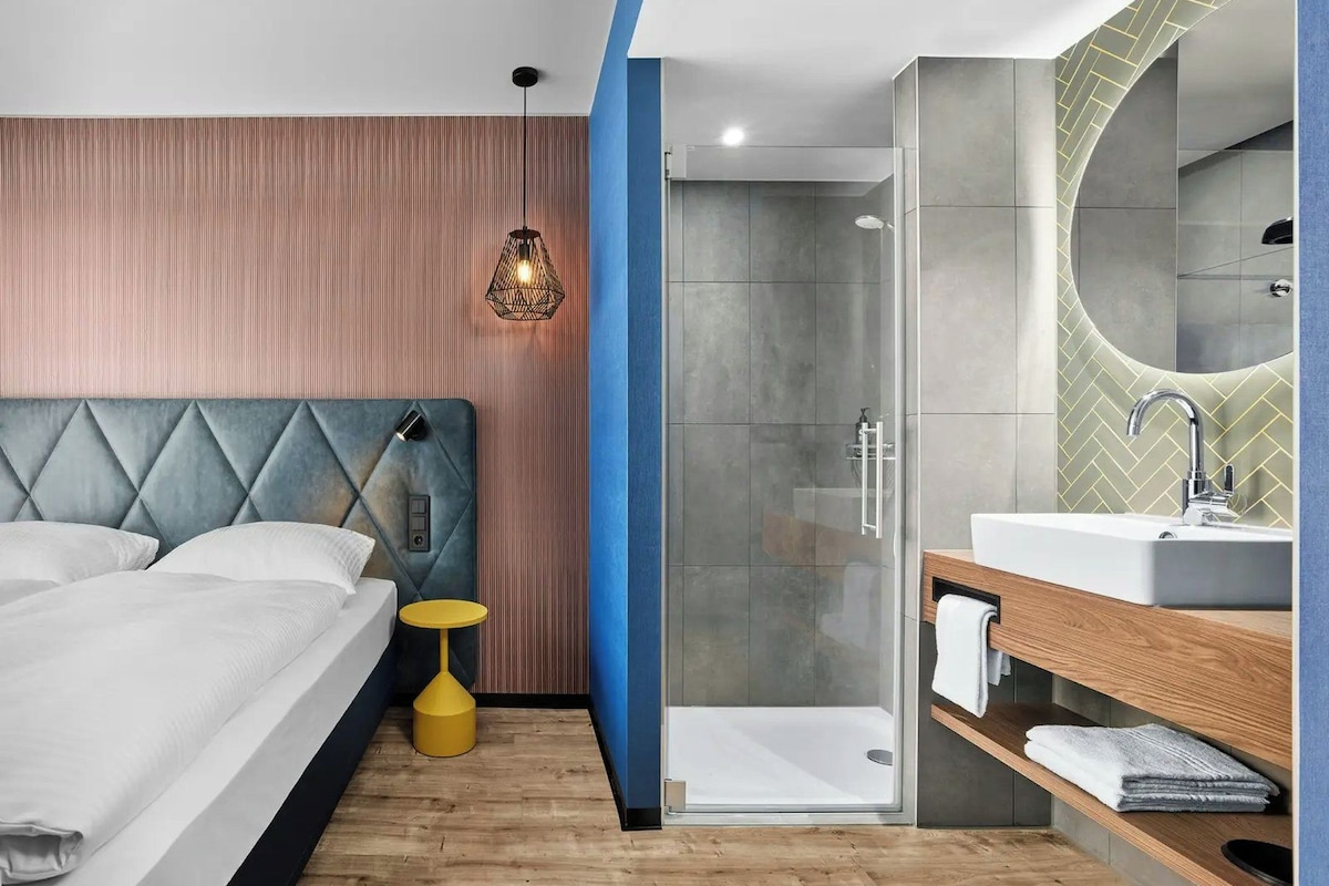 Un dormitorio moderno con cama, mesita de noche y ducha a pie.
