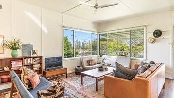 A spacious living room with a large window, a ceiling fan, and a bookshelf.