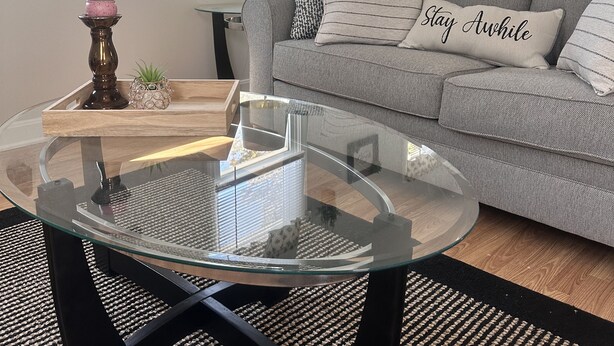 Una sala de estar con una mesa de centro de vidrio, un sofá gris y cojines decorativos.