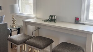 Un salón acogedor con un sofá blanco, una mesita redonda con una lámpara y una ventana con persianas.