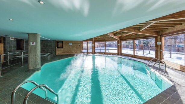 Ein Hallenbad mit klarem Wasser, Holzbalken und großen Fenstern.