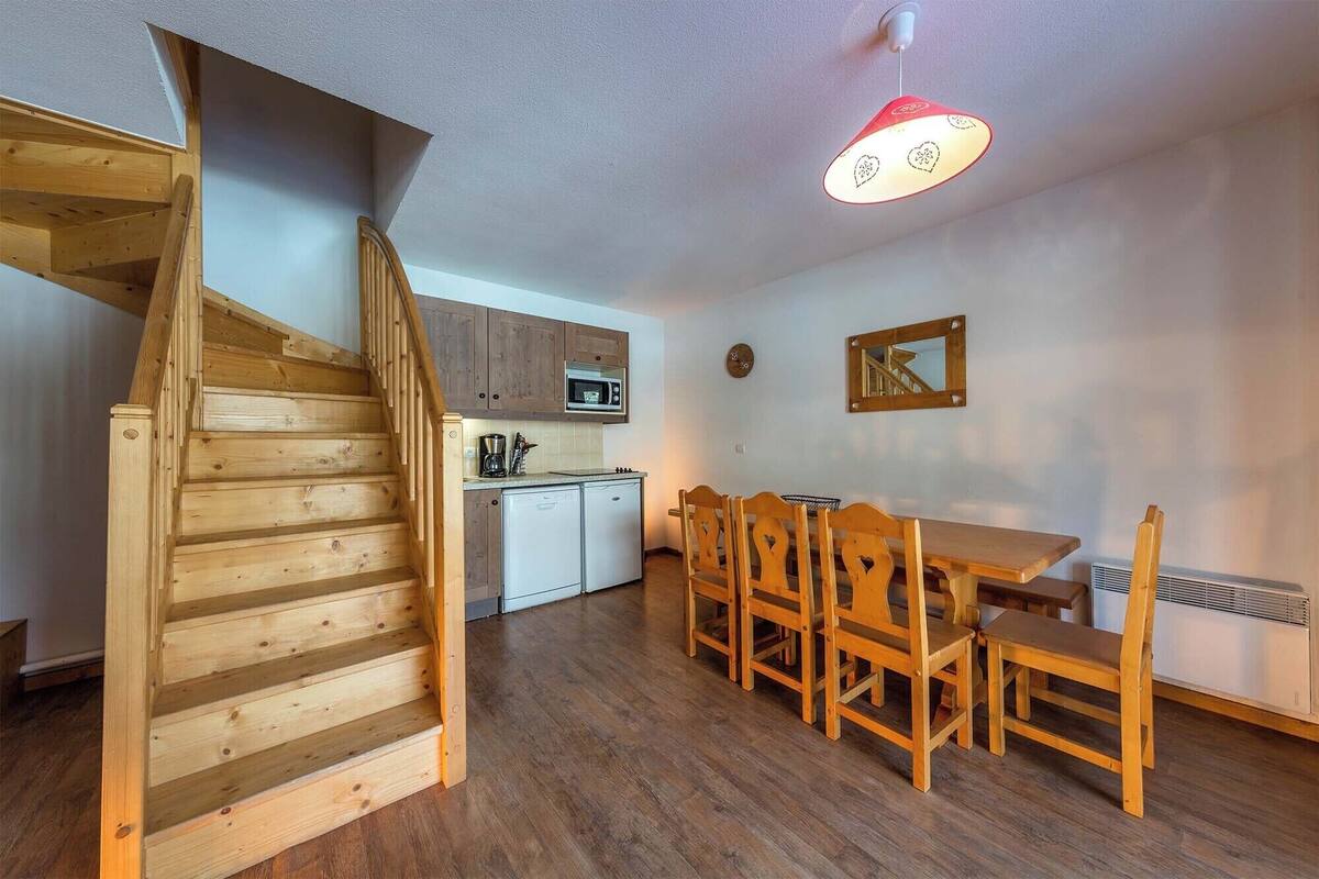 A wooden staircase leading to a kitchen with a microwave, a dining table with chairs, and a red pendant light.