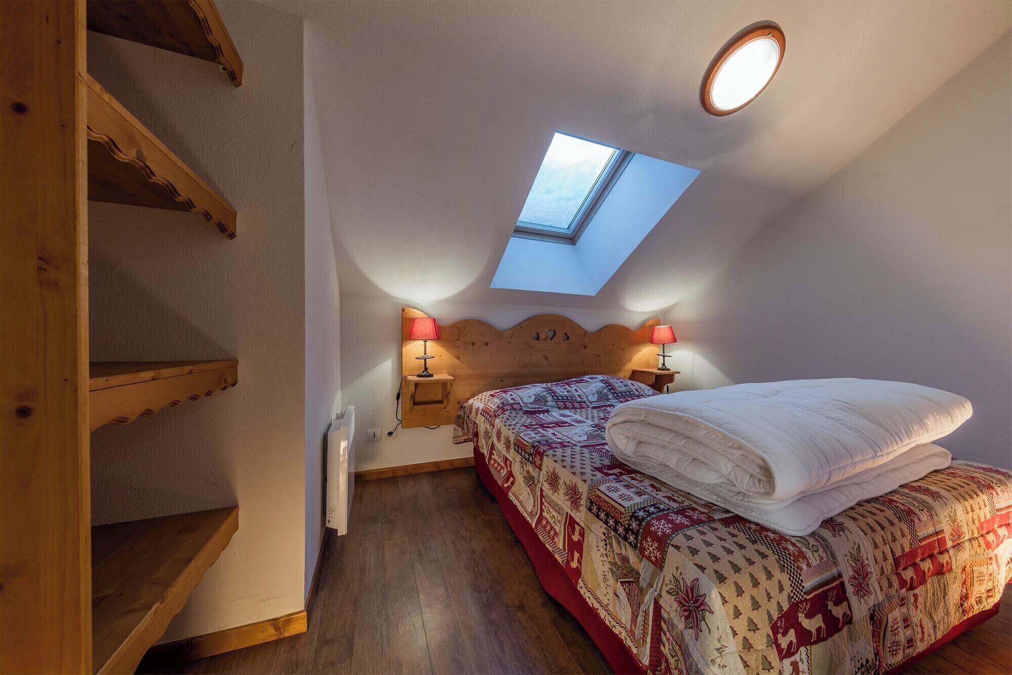 Une chambre à coucher avec un puits de lumière, une tête de lit en bois, deux lampes de chevet, une couvre-lit à motifs et un lit parfaitement fait.