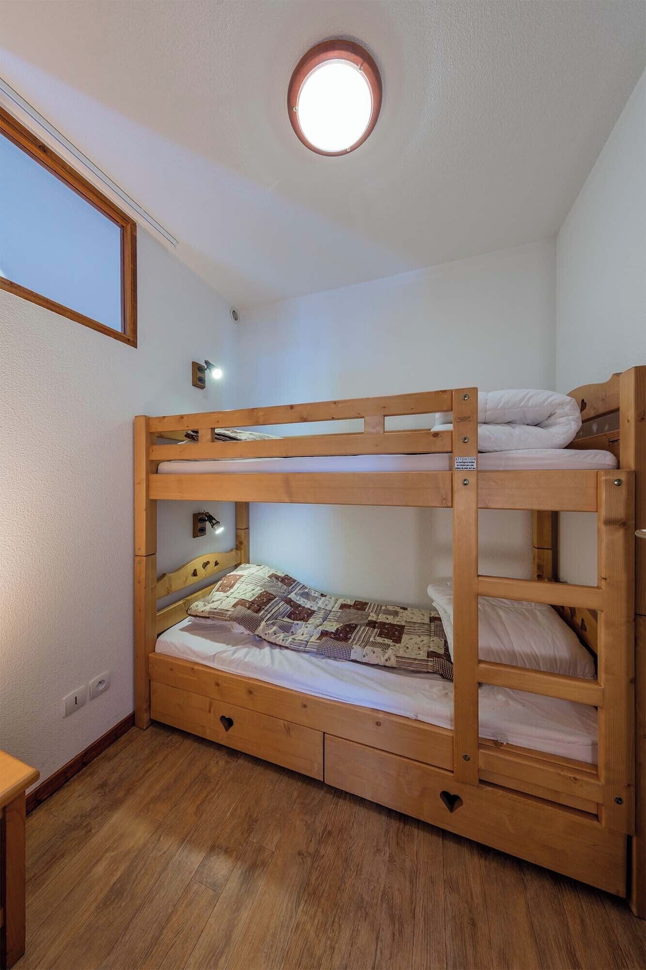 Une chambre avec un lit superposé, une lucarne et un petit bureau.