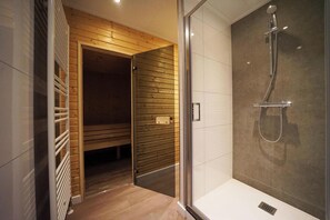 Bathroom features a shower with a glass enclosure and a chrome showerhead, alongside a wooden bench for seating.