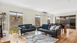 A spacious living area with two black leather sofas, a glass coffee table, and a wooden dining table.