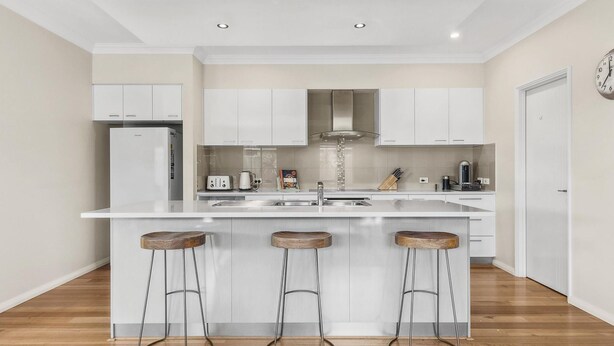 A modern kitchen with white cabinetry, a central island with stools, a built-in oven, and a stainless steel range hood.