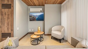 Habitació moderna amb sostre de fusta, aire condicionat fixat a la paret, finestra gran amb cortines, sofà, cadira i taula petita amb un objecte decoratiu.