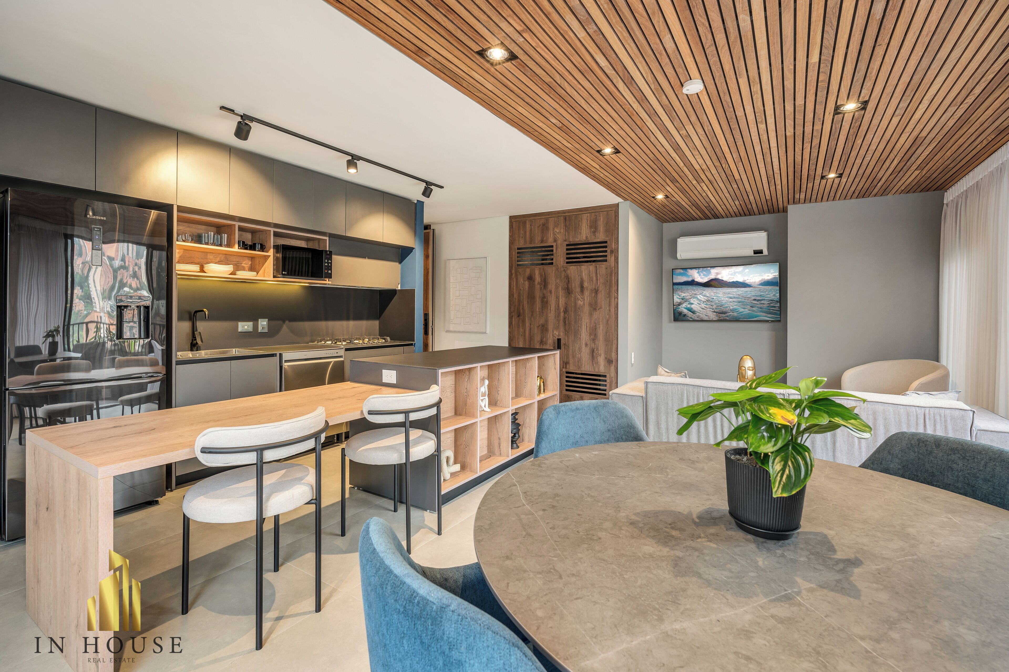 A modern kitchen with built-in appliances, a dining area with a round table and blue chairs, and a wooden ceiling.