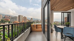 Un balcó amb vista a la ciutat, una zona de menjador amb taula i cadires, i una banca de fusta.