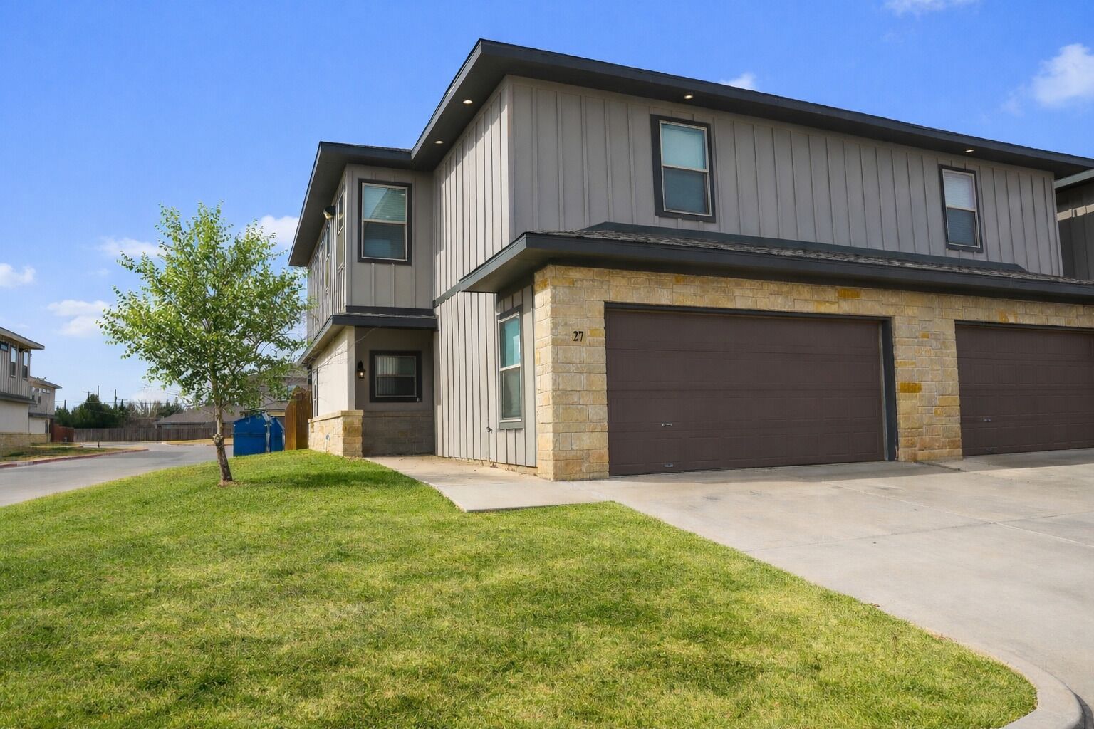 A two-story residential building with a garage, a well-maintained lawn, and a clear blue sky.