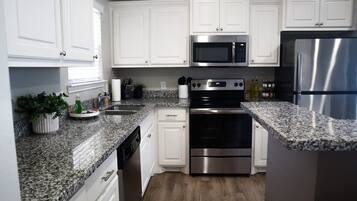 A modern kitchen with white cabinets, granite countertops, stainless steel appliances, and a dishwasher.