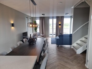 Relax in a spacious living area with a dining table and comfortable seating, featuring a chandelier and large windows with a view.