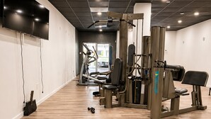 Un gimnasio con equipo de ejercicio, una banca y un televisor en la pared.