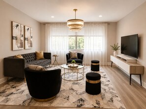 A modern living room with a sofa, armchair, ottoman, coffee table, and a TV.