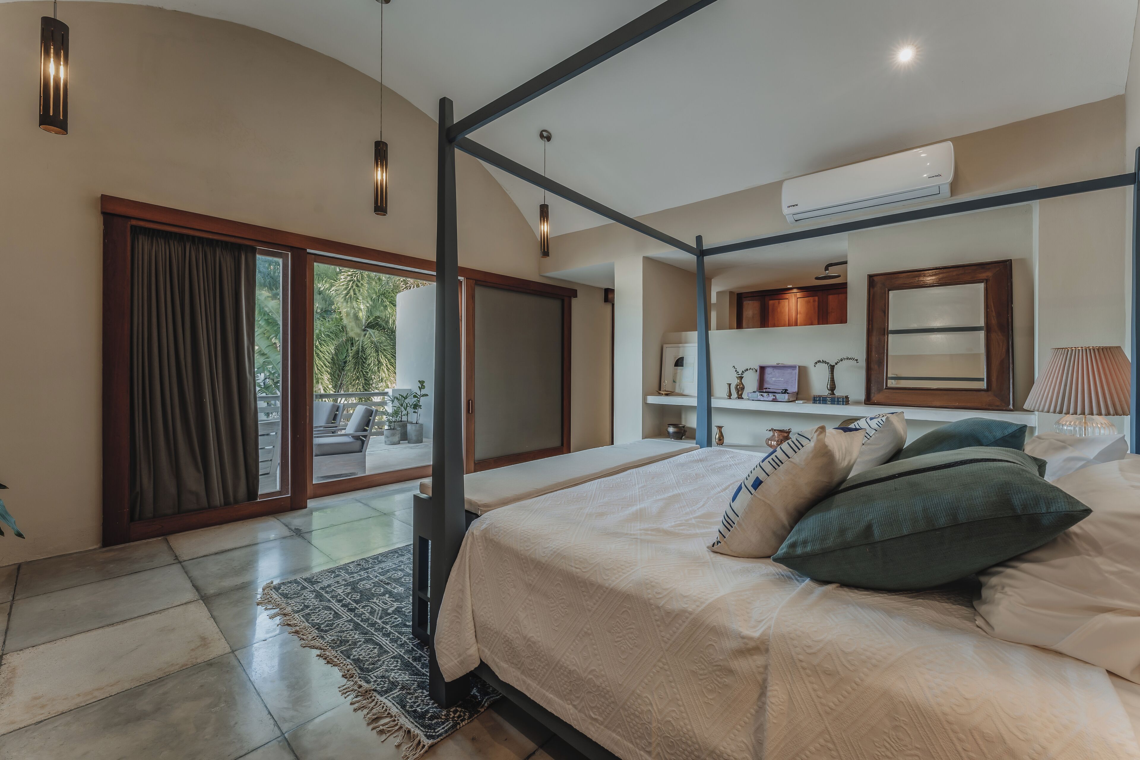 Une chambre à coucher avec un grand lit, un ventilateur de plafond, une fenêtre avec des rideaux, une petite table et une table de chevet.