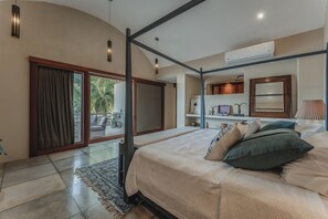 A bedroom with a large bed, a ceiling fan, a window with curtains, a small table, and a nightstand. - Casa Exclusiva Los Amigos, 4BDR by Cercana (Mérida)