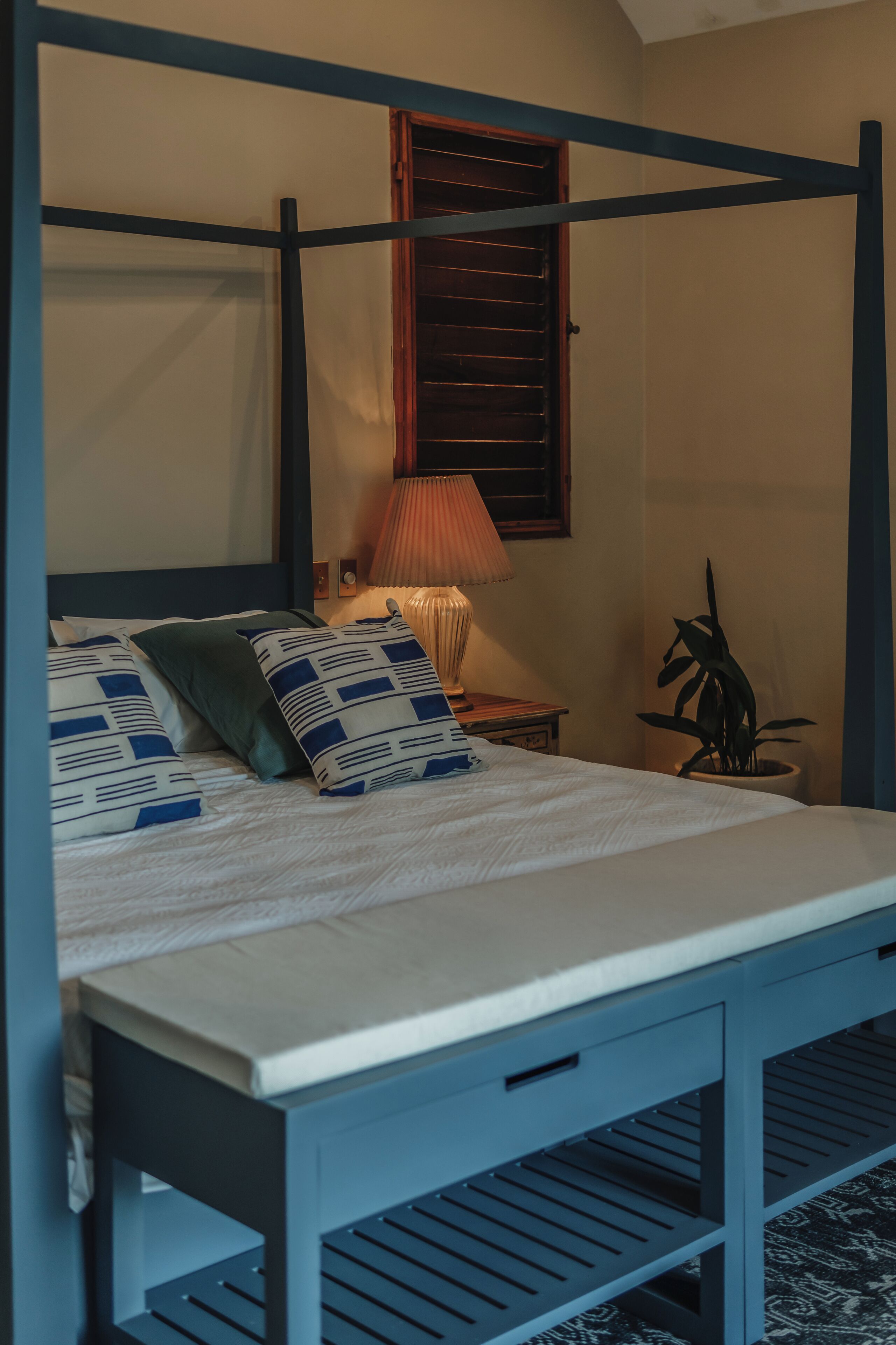 A bed with a wooden frame, a bedside lamp, and a potted plant.