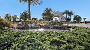 A landscaped garden with a water feature, palm trees, and a building with an arched entrance. - Enjoy Resort living in the Upscale Lakewood National Golf Country Club community (Bradenton)