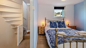 A bedroom with a bed, bedside tables, a window with a view, and a staircase. - 2 Bed in Brixham (oc-p30465) (Brixham)