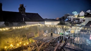 A rooftop terrace with a wooden table, chairs, and a bottle of wine. - 2 Bed in Brixham (oc-p30465) (Brixham)