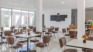 Een moderne eetruimte met tafels en stoelen, een menubord en een keuken op de achtergrond.