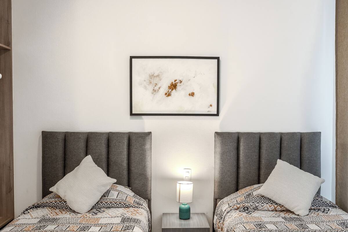 Habitación de hotel con dos camas, cada una con ropa de cama estampada y cabecero. Un cuadro abstracto enmarcado cuelga de la pared sobre las camas.