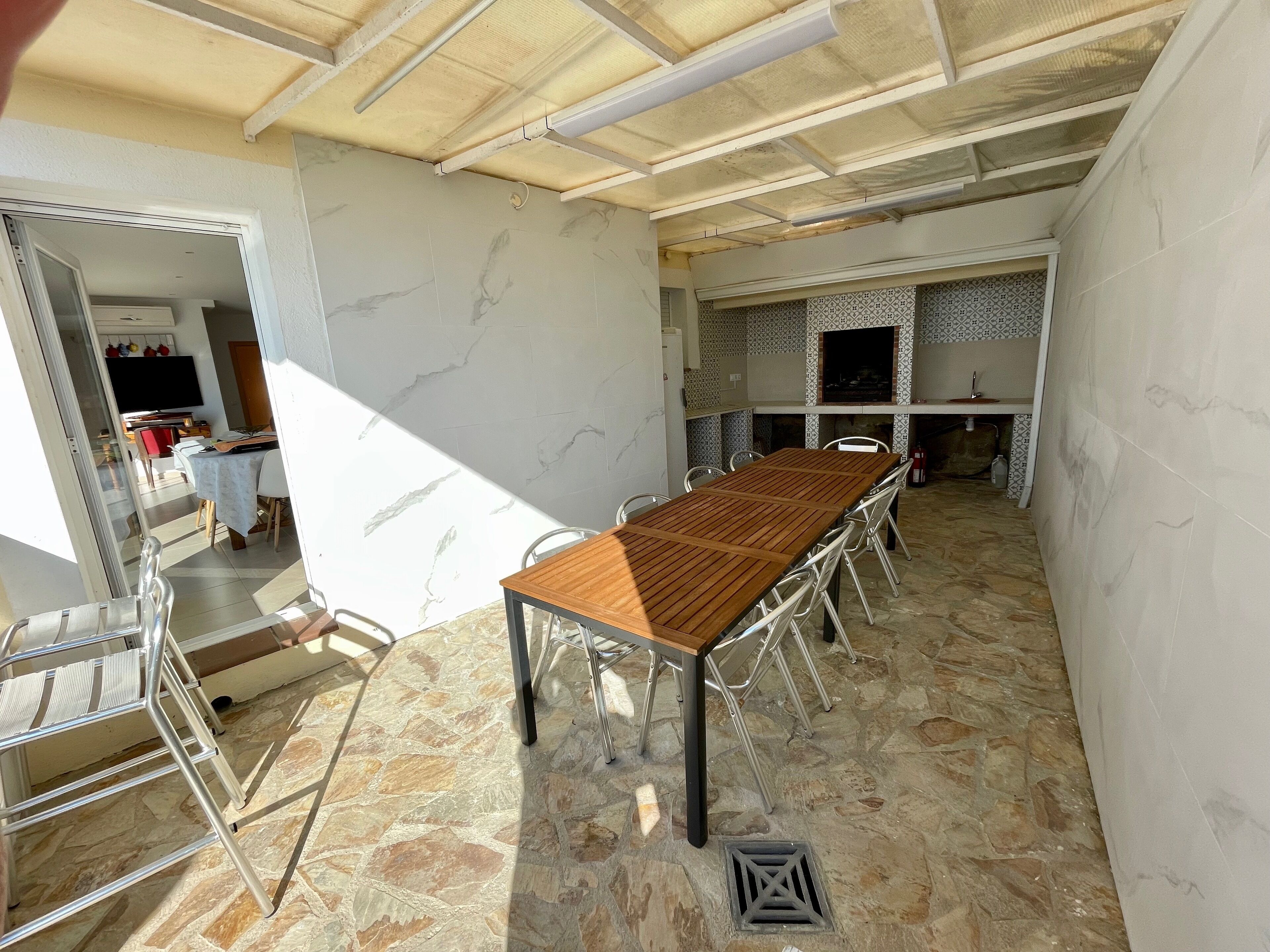 A spacious room with a long wooden table and metal chairs, a stone floor, and a tiled backsplash in the kitchen area.