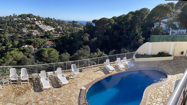 Zona de piscina con sillones de descanso y terraza de baldosas de piedra, con vistas a una colina panorámica.