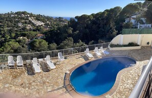 Ein Poolbereich mit Liegestühlen und einer terrasse mit Steinplatten, umgeben von einer schönen Hügellandschaft.
