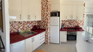Una cocina compacta con armarios blancos, encimera roja, microondas, refrigerador y estufa.