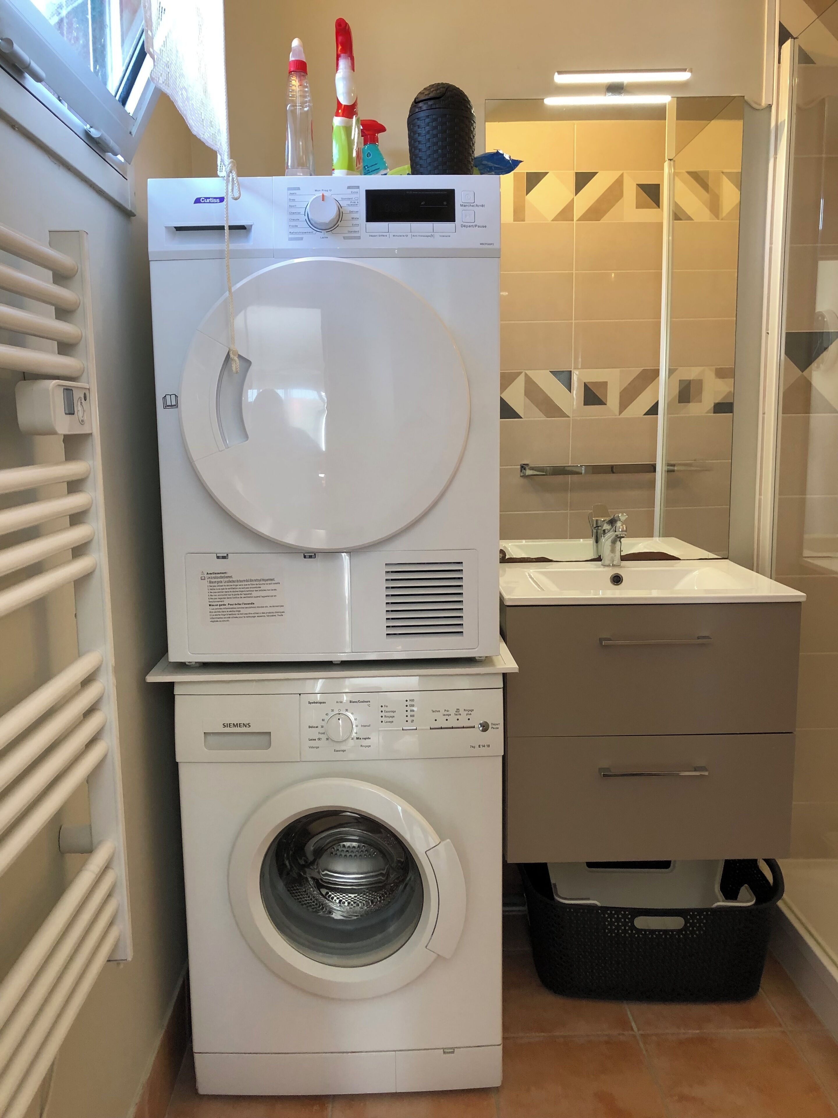 Un espace buanderie compact comprenant un lave-linge et un sèche-linge superposés, un évier et un miroir.