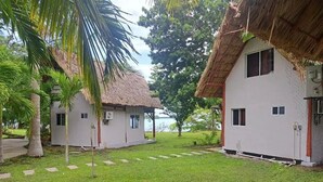 Un bungalow doté d’un toit de chaume, entouré d’une végétation luxuriante et offrant une vue dégagée sur l’eau.