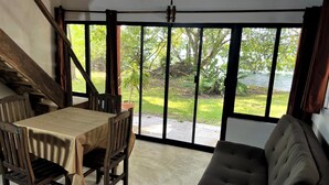 Une pièce comprenant une table à manger et des chaises, un canapé et de grandes fenêtres donnant sur un jardin et une étendue d’eau.