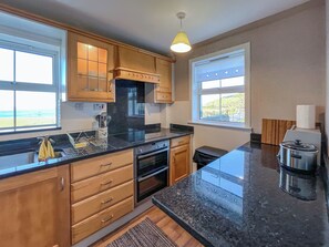 Una cocina moderna con armarios de madera, encimera negra y vistas a la playa.