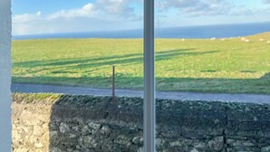 Blick aus einem Fenster auf ein grünes Feld mit einer Steinsäule und blauem Himmel.