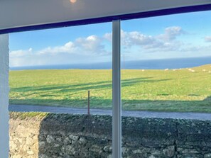 Blick aus einem Fenster auf ein grünes Feld mit einer Steinsäule und blauem Himmel.