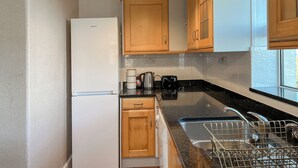 Eine kleine Küche mit Holzausstattung, einem weißen Kühlschrank, einer Kaffeemaschine und einem Spülbecken mit Geschirrgestell.