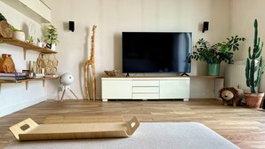 Un salon moderne avec un plancher en bois, un téléviseur à écran plat, un canapé, une table basse en bois, une bibliothèque et divers objets de décoration, notamment une girafe, un lion et des plantes en pot.