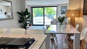 Une cuisine moderne équipée d’une cuisinière à gaz, de meubles blancs et d’un coin repas avec une table en verre et des chaises blanches.