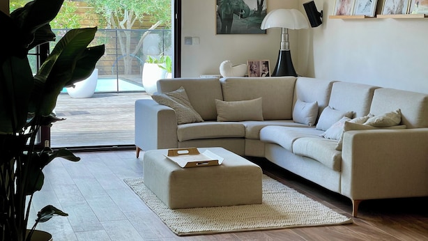 Un salon moderne avec un canapé d’angle beige, une petite table basse et une grande plante en pot.